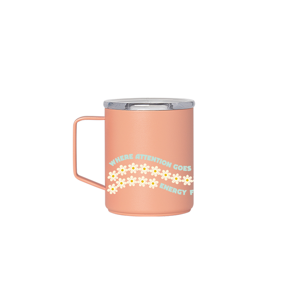 A peach camp mug with the phrase "Where attention goes, energy flows" with daisies trailing the phrase.