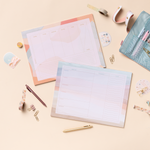 A Many Moons Tearaway desk pad and a Sunset striped Tearaway desk pad. Both have a weekly calendar spreads. Displayed with jotter pens, stickers, and washi tape.