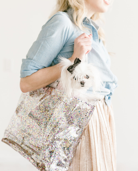 Woman stands holding confetti tote with a white dog inside. 