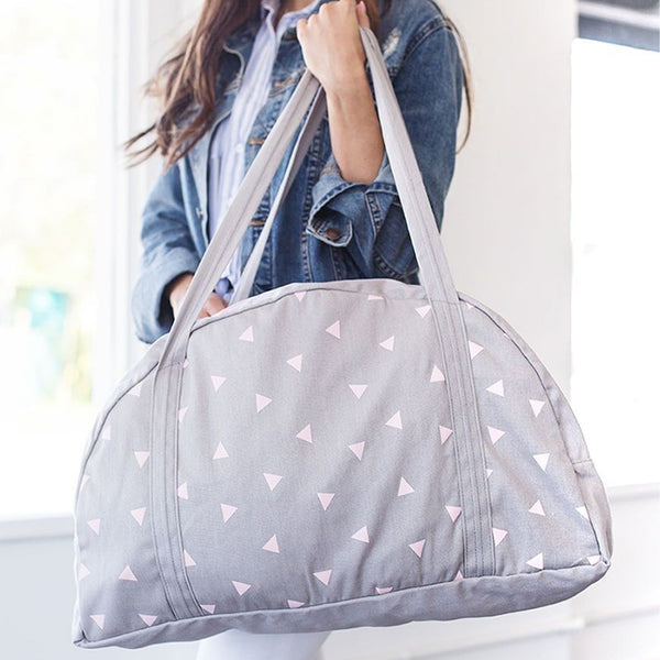 Smiling girl holding a cute carryon bag in gray canvas with triangle pattern.