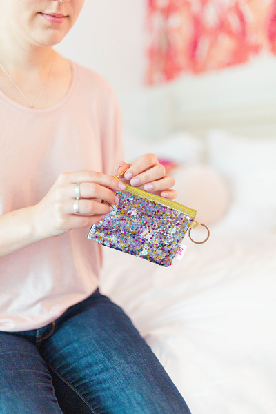 A woman holding a pouch with a ring that can be attached to a bag or key ring, large enough to fit cards or small necessities  