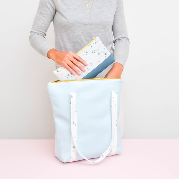 Girl holding a cute tote bag in light blue vegan leather with white paint splatter straps and zippered top.