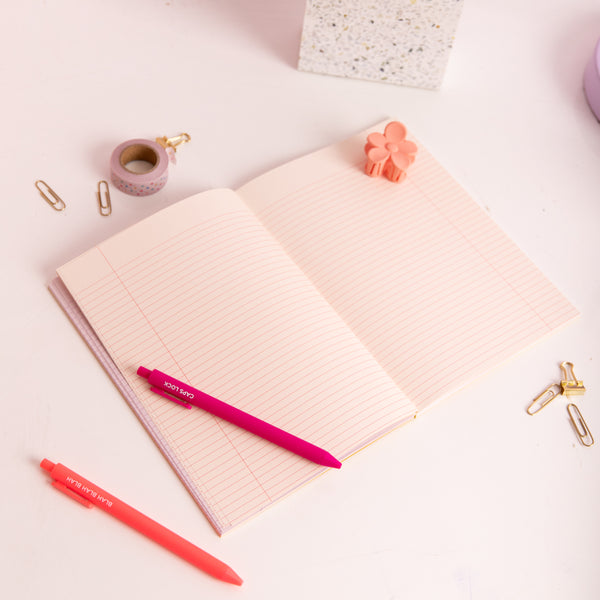 Peach Feminist Agenda notebook opened to lined pages with coral and pink jotter pens