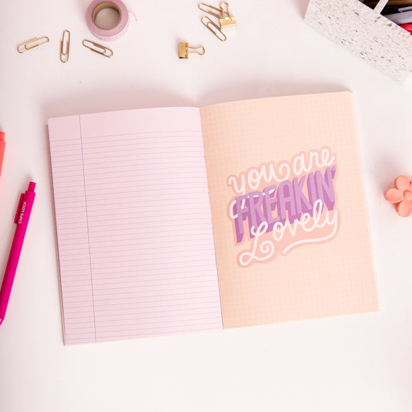 Peach Feminist Agenda notebook opened to lined and "Your Freaking Lovely" tip-in pages with coral and pink jotter pens
