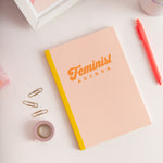 Peach Feminist Agenda notebook closed with coral jotter pen