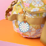 Gold plated key charm with blue background and a white daisy hanging off a flower duffle bag.