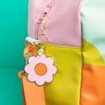 Gold plated key charm with pink flower and middle center hanging off a multi-colored bag.