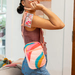 Girl wearing the pink with rainbow waves portrait crossbody while holding a key ring on her finger.