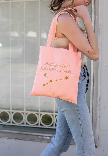 Lady carrying our Peach canvas tote with "SORRY OUR ZODIACS JUST AREN'T COMPATIBLE" in shimmer gold.
