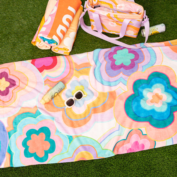 Colorful trippy flower pattern beach towel laying on grass with misc items.