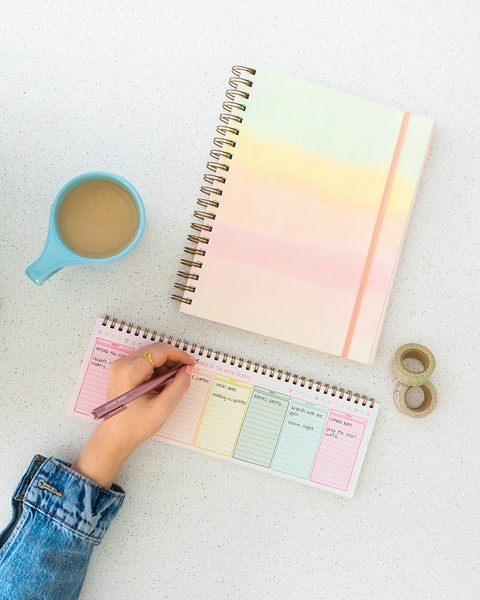 Hand filling out the colorful fresh start weekly planner next to her coffee. 