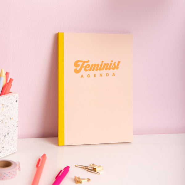 Peach Feminist Agenda notebook closed with coral jotter pen