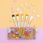 Clear flower power pouch with paint brushes inside. Orange and pink background with small flowers.