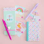 Small mint green taskpad with colorful hearts on the binding and text that reads Make It Happen on the cover. Next to it a rainbow sticker, narwhal sticker and "Quit with the Doubt" sticker. A small notebook covered in tiny mulitcolor hearts and a baby blue spine.
