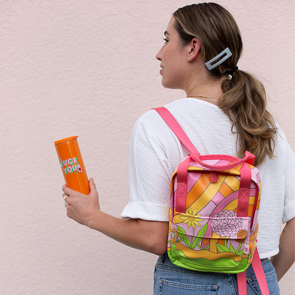 woman holding an orange fuck you tumbler carrying a mini backpack in the groove pattern over her left shoulder.