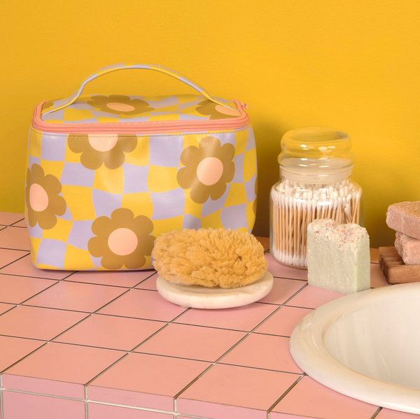 Mustard yellow background with medium light violet and green checker pattern with flowers soulmate along with misc items on a pink squared surface 