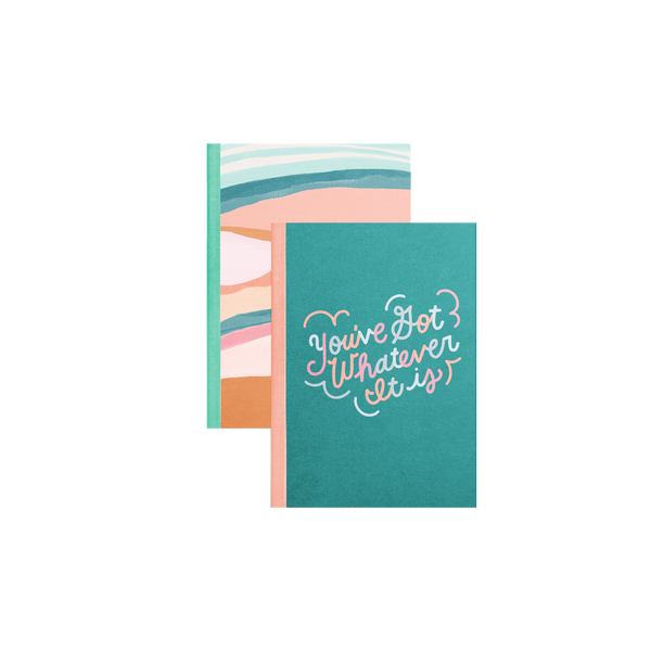 A teal notebook with a light pink spine with the phrase "You got whatever it is" printed on the front in multicolored pastel lettering, on top of another notebook with a multicolored pastel abstract landscape design and a light teal notebook spine.
