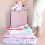 Ice cream social packing cubes with clothes stacked. Woman packing shoes in smallest cube on top of a pink suitcase.