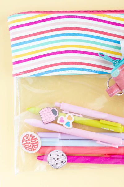 A clear vinyl pouch with curvy, rainbow lines on the top, three greeting cards sets in pink and green, and a Coral Pink, Luxardo, and Bright Blue color Jotter pen.