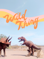A print with the phrase "Wild thing" printed on in orange, cursive lettering. Behind the lettering is a pink and yellow wave-like line. Background of print is a picture of the desert and a T-Rex and a Triceratops 