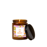 Amber glass candle jar with sticker on front with multi-color wavy and floral design and text that reads "IT'S ALL GROOVY" in orange font in a white square.