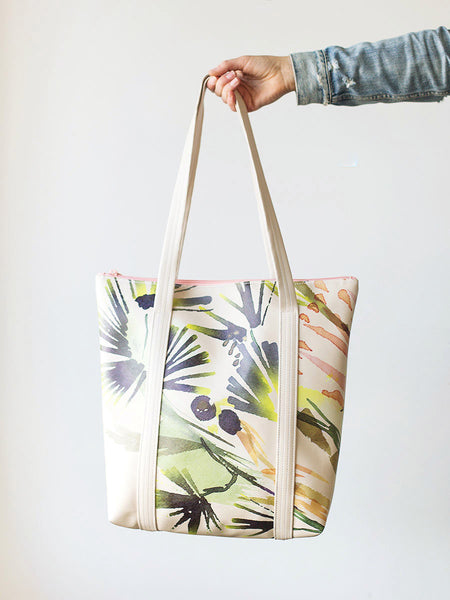 Woman's hand holding a cute tote bag in tropical print vegan leather.