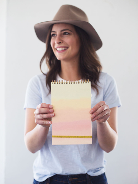 A happily smiling young woman holding a taskpad with a soft rainbow gradient in front of her.