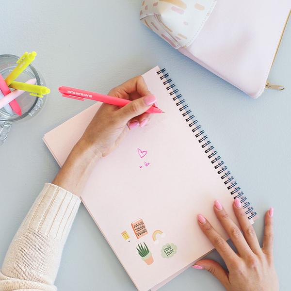 Overhead image of a left-handed woman with pink fingernails doodling in a pink planner.
