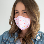 A brunette wears a pink facemask with small rainbow illustrations.