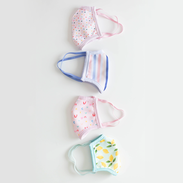 A flat lay of four face masks. An ombre lemon face mask, a pink face mask with rainbows, a lightly striped face mask and a pink face mask with tiny hearts illustrated all over. 